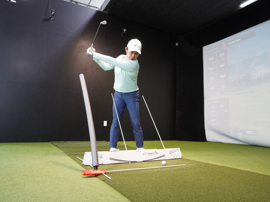 Face-on view of a golfer at the top of the backswing with a standing noodle beside her hip and the V6 noodle in front