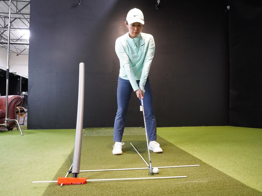 A golfer standing in a grid of alignment sticks showing target line, feet line and ball position