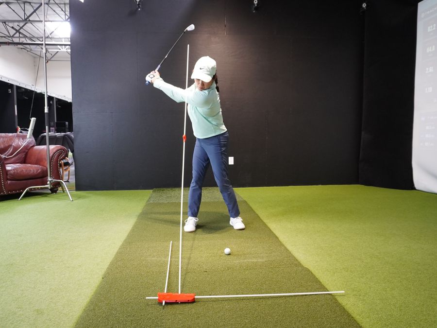 Face-on view of a golfer with two alignment sticks joined by the extender connector, standing tall beside her head